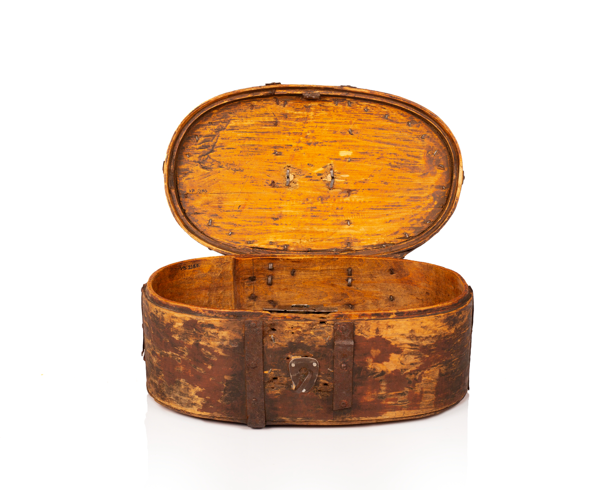 Brun bomme med lås og nøkkel. Den er ovalformet med et svakt hvelvet lokk som er festet med hengsler. Bunnen av bommen er plan. Videre er både bunnen av bommen og toppen av lokket laget av gran, mens sidene er laget av bjørk. 

Lokket og bommens sider er sveipet og består av tynne bjørkelapper, i relativ kraftige dimensjoner, som er brettet sammen for å danne bommens form. Bjørkelappen overlapper hverandre med en god del cm på baksiden og er festet med dobbel nagling. Det er fire nagler i hver av de to rekkene som fester siden sammen. De to rekkene står parallelle overfor hverandre med ca. 5 cm mellomrom. Siden til lokket er festet med en nagle i hver rekke, og i tillegg er det satt inn en nagle nederst på bommen mellom de to rekkene samt en i lokket. 

To smidde jernbånd går fra fremsiden av bommen over lokket og ned på baksiden. På baksiden er det satt inn løkkehengsler i jernbåndene til lokket. Båndene er satt på plass med jernnagler. Rundt toppen av lokket er det et jernbånd som fester lokkets topp og side sammen. Båndet er bøyd over siden, festet med nagler og dekorerte med innovervendte tagger. Midt på bommens lokk er det et håndtak som er festet med nagler. Det er i tillegg jernbånd som går ned på hver side av bommen, disse strekker seg ikke over lokket. 

Bommen har en smidd lås med et hjerteformet nøkkelskilt, og en tilhørende nøkkel. Man kan se rester av brun oljemaling på utsiden av bommen. 