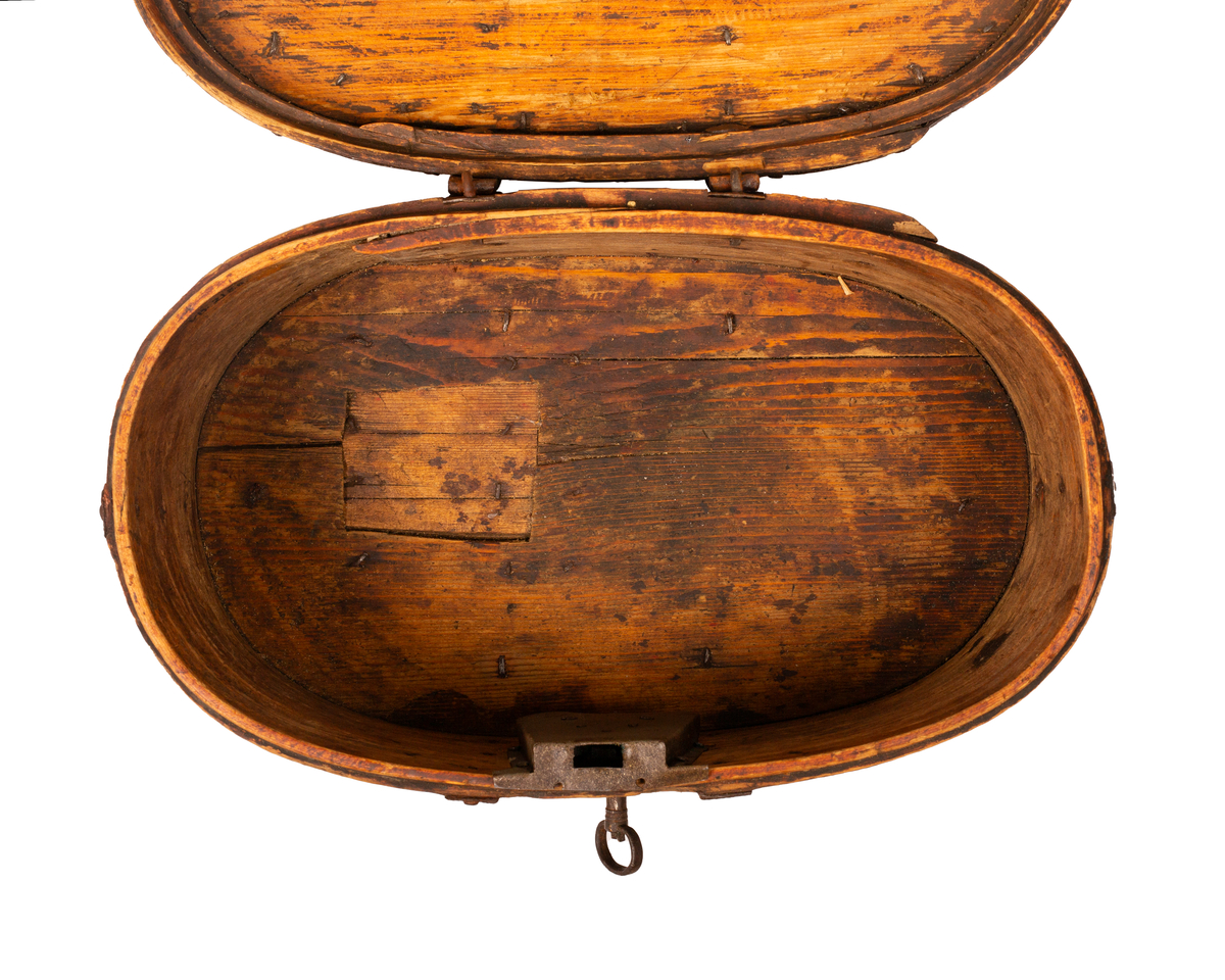 Brun bomme med lås og nøkkel. Den er ovalformet med et svakt hvelvet lokk som er festet med hengsler. Bunnen av bommen er plan. Videre er både bunnen av bommen og toppen av lokket laget av gran, mens sidene er laget av bjørk. 

Lokket og bommens sider er sveipet og består av tynne bjørkelapper, i relativ kraftige dimensjoner, som er brettet sammen for å danne bommens form. Bjørkelappen overlapper hverandre med en god del cm på baksiden og er festet med dobbel nagling. Det er fire nagler i hver av de to rekkene som fester siden sammen. De to rekkene står parallelle overfor hverandre med ca. 5 cm mellomrom. Siden til lokket er festet med en nagle i hver rekke, og i tillegg er det satt inn en nagle nederst på bommen mellom de to rekkene samt en i lokket. 

To smidde jernbånd går fra fremsiden av bommen over lokket og ned på baksiden. På baksiden er det satt inn løkkehengsler i jernbåndene til lokket. Båndene er satt på plass med jernnagler. Rundt toppen av lokket er det et jernbånd som fester lokkets topp og side sammen. Båndet er bøyd over siden, festet med nagler og dekorerte med innovervendte tagger. Midt på bommens lokk er det et håndtak som er festet med nagler. Det er i tillegg jernbånd som går ned på hver side av bommen, disse strekker seg ikke over lokket. 

Bommen har en smidd lås med et hjerteformet nøkkelskilt, og en tilhørende nøkkel. Man kan se rester av brun oljemaling på utsiden av bommen. 