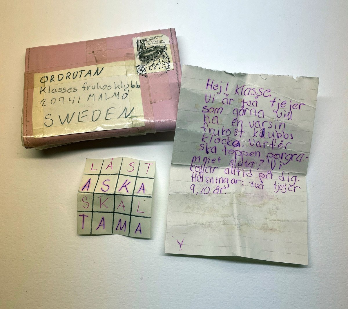 Plånbok i rosafärgat konstläder. Plånboken är adresserad till Ordrutan Klasses frukostklubb.  Frankerad med ett frimärke. 

På insidan står det Föreningsbanken i vit text. I plånboken liggger två skolfotografier på Helene och Lizette som är avsändarna. I sedelfacket finns två papperslappar fasttejpade med deras adresser. I myntfacket svar på ordrutan / rebus. I annat fack ett brev.
