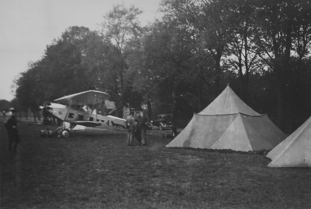 Flygtekniker i samtal vid vitmålat militärflygplan S 6 Fokker på ett flygfält vid manöver i Skåne, omkring 1935-1937, Tält uppslagna vid platsen. Flygplanet har en målning av en räv. 

Text vid foto: "Manöver i Skåne"