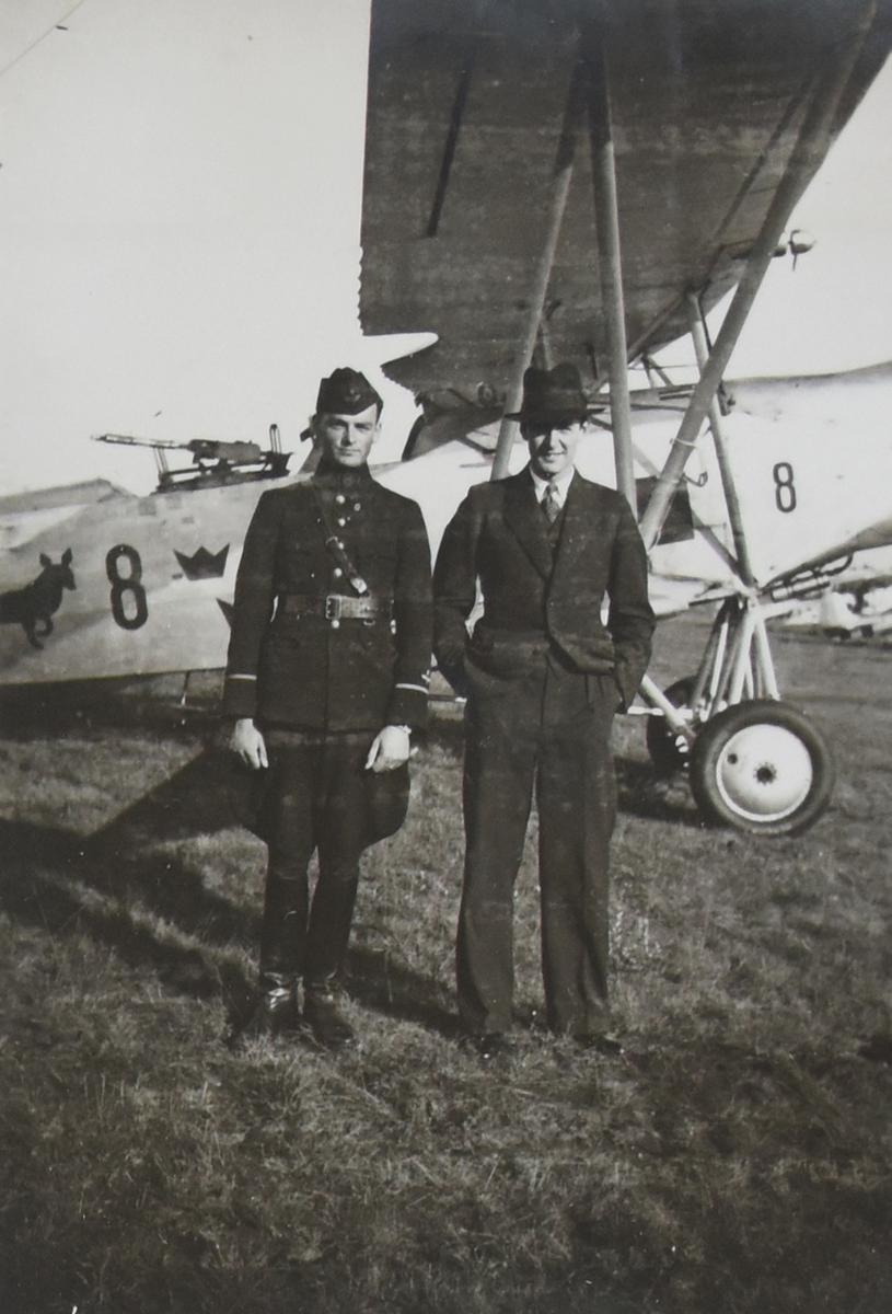Porträttfoto av två män framför militärt flygplan S 6 Fokker på ett flygfält. Till vänster, militärflygare Nils-Olof Sefeldt, till höger en okänd civilklädd man. Vid manöver i Skåne, omkring 1935-1937.

Text vid foto: "Efter manövern"