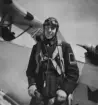Porträtt av militär flygförare i flygdräkt framför flygplan. Omkiring 1934-1937.

Text vid foto: 