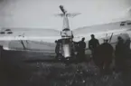 Folksamling vid militärt flygplan Sk 11 som landat på nosen på ett fält, omkring 1934-1937. Vy framifrån.

Text vid foto: 