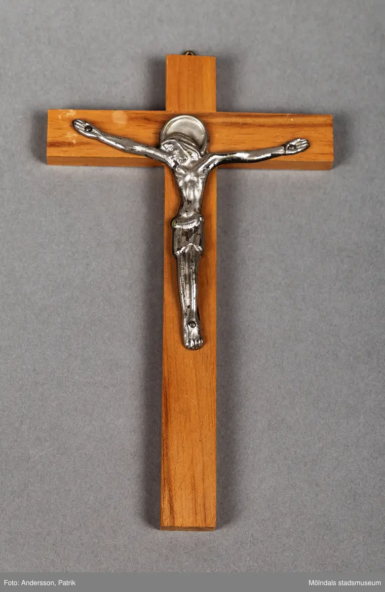 Ett kors i trä med en jesusfigur i metall hängande på korset. Längst upp på korset finns en hake för upphängning. Korset är en konfirmationsgåva. Alla konfirmander i givarens grupp fick denna konfirmationsgåva.
