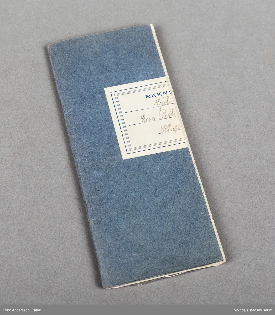 Ett blått räknehäfte som är vikt i mitten. Sidorna som är vikta, bildar fickor där bokmärken har förvarats. Sidorna i boken har rutor och avsett för räkning. Boken har använts för byte av bokmärken mellan klasskamrater. Man stoppade i en av sidorna på måfå och bytte eller blev av med sitt bokmärke.