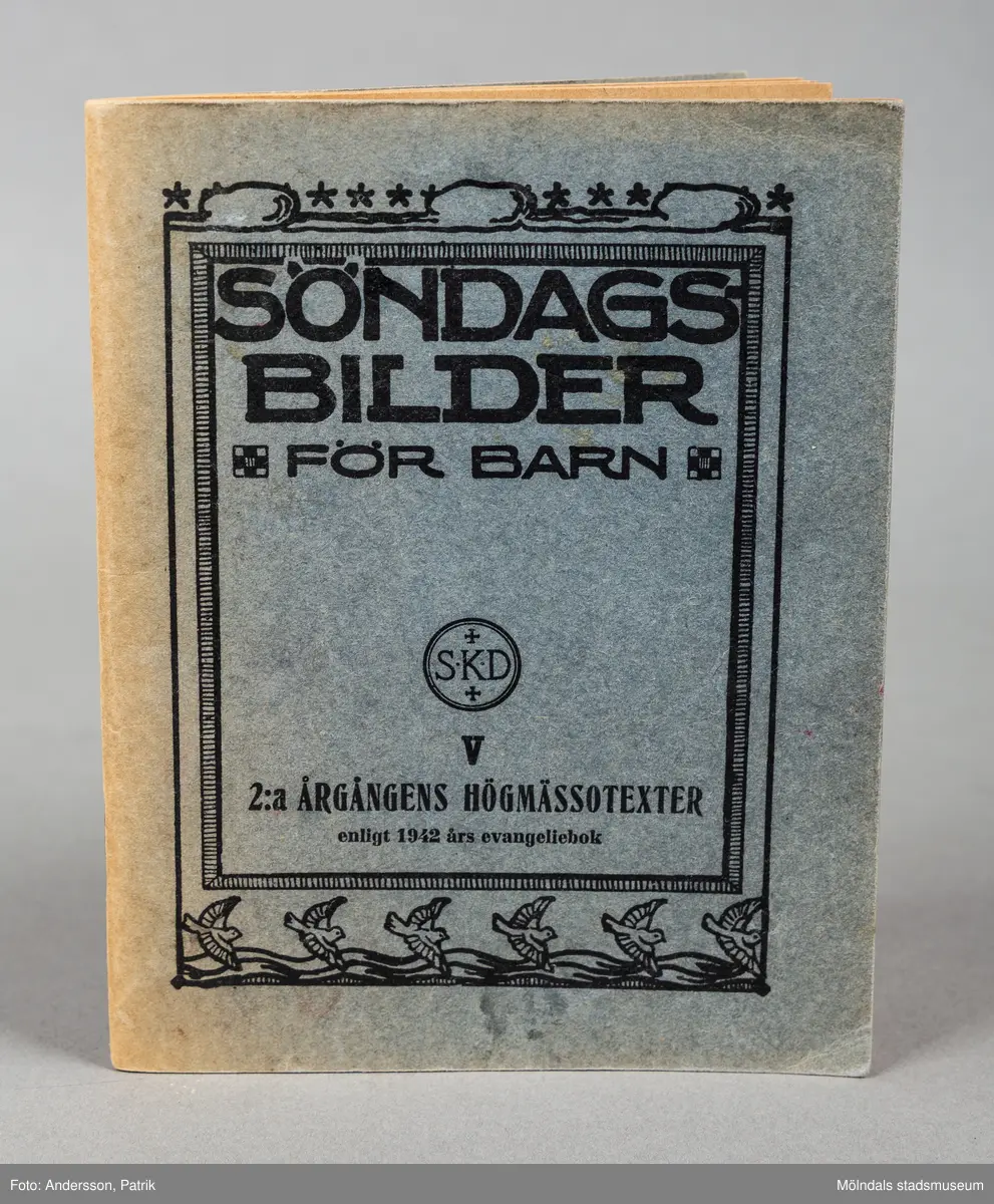 Ett häfte med mjuk pärm. Häftet är blått med svart påförd text. Runt texten finns en svart ram kantad av illustrationer i form av flygande duvor, vågor och mösnster. På häftets baksida finns en priset på 1 krona (med bilderna) angivet. Boken användes i söndagsskolan och har inklistrade bilder med religiösa motiv ur bibeln.
