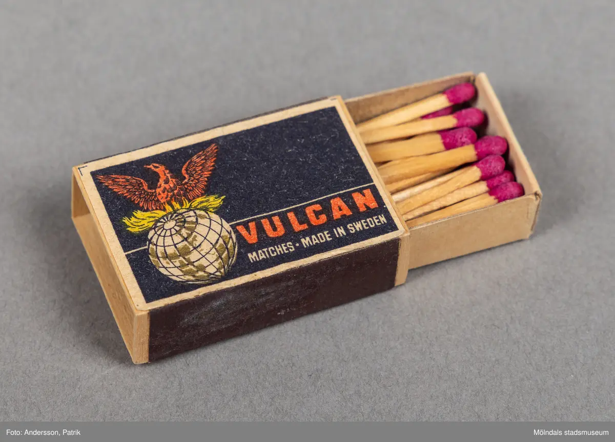 En liten tändsticksask av märket Vulkan. Asken är svart med cremefärgad ram i ytterkanten. På asken finns en bild av en jordglob varpå en röd fågel sträcker ut vingarna. Vulcans tändsticksfabrik grundades av Von Essen släkten 1868. Omkring 1900 var Vulcan världens största tändsticksproducent. År 1903 slog fabriken Vulcan ihop med Jönköpings tändsticksfabrik, Annebergs tändsticksfabrik till Jönköpings och Vulcans tändsticksfabrik.