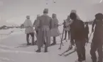 Vinterövningar på 1940-talet. Trupp på skidor rastar, hus i bakgrunden, nyfikna barn i förgrunden.