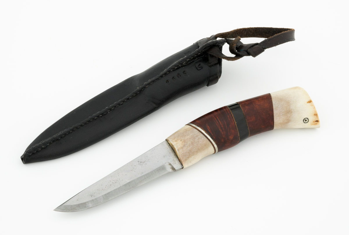 Tollekniv i slire, der knivskaftet og slira er lagd av den danske etnologen, museumslederen og knivmakeren Henrik Vensild, som i mange år besøkte Norsk skogmuseum og det såkalte «knivtorget» under De nordiske jakt- og fiskedager.

Kniven er 20,0 centimeter lang, målt fra bladspissen til og med knappen i ytterenden av skaftet. Bladet er 9,1 centimeter langt og snaut 2,3 centimeter bredt ved brystningen (overgangen til skaftet). Her er bladtjukkelsen om lag 3,7 millimeter, men den avtar noe framover mot knivspissen. Umiddelbart bak slipefasen der er tjukkelsen snaut 2,6 millimeter. Overflata på bladet har den noe rue overflata den fikk av hammeren på ambolten intakt, men disse flatene er polerte. Bakerst på høyre side finner vi et stempel, «Steen N.», som er stempelet til den danskfødte smeden Steen Nielsen, som lenge har bodd i Kristiansand. Bladryggen er planslipt, men er samtidig noe avrundet i den fremre enden. Slipefasene er opptil 6,5 millimeter brede.

Skaftet er nesten 10,5 centimeter langt. Det buer noe nedover (mot skaftbuken) i den bakre enden og har, som knivblader flest, et ovalt tverrsnitt. Sett i lengderetningen er den midtre delen av denne knivdelen noe konveks. Skaftet er sammensatt av flere komponenter. Fremst, mot bladet, er det en del av horn, antakelig reinsdyrgevir. Den enden som vender mot bladet er rett (butt), den andre enden er skrått avskåret. Mot denne flata er det lagt ei lærforing, deretter ei sølvplate og så nok ei lærforing. Deretter følger et stykke brunt, mønstret tre, en svart ring av et ibenholtliknende materiale. og nok et stykke av det brune, mønstrete treet. Ytterenden er skråskåret. På den skrå endeflata er det lagt nok ei lærforing, denne gangen uten noe metallinnlegg, mot endetappen, som er av reisdyrhorn. På denne komponenten er det to små ringer med et punkt i sentrum, en slags signatur for Henrik Vensild. Tangen fra knivbladet er ført gjennom hele skaftet. Den bakre enden av denne jernteinen er klinket mot noe som later til å være en messingring.

Slira er sydd av mørkebrunt lær. Den er cirka 16,9 centimeter lang (uten beltestropp) og 3,4 centimeter bred (målt på midten). Slireformen er symmetrisk, når man ser bort fra at overkanten er skrått avskåret. Den nedre delen, som skal omslutte bladet, er nokså flattrykt, mens den øvre delen, som skal omslutte nedre del av skaftet, er mer rundoval. Sliras forside er dekorert med to parallelle linjer i lengderetningen med innstemplete små treflikete blader med noenlunde regelmessig innbyrdes avstand. Dette dekorelementet er, åpenart med hensikt, plassert på en måte som bryter litt med den nevnte symmetrien. Like under sliremunningen er det skåret små spalter i slirelæret. Her er det inntredd ei cirka 9 millimeter bredt lærreim, som også er tredd gjennom ei spalte i et «øre» på den øvre delen av sliresømmen. Endene på den nevnte lærreima er knyttet sammen slik at den danner ei løkke som kan tres inn på et belte. Henrik Vensild har stemplet inn initialene sine og produksjonsåret - 2005 - på baksida av sliras overdel.