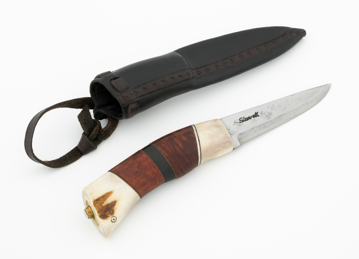 Tollekniv i slire, der knivskaftet og slira er lagd av den danske etnologen, museumslederen og knivmakeren Henrik Vensild, som i mange år besøkte Norsk skogmuseum og det såkalte «knivtorget» under De nordiske jakt- og fiskedager.

Kniven er 20,0 centimeter lang, målt fra bladspissen til og med knappen i ytterenden av skaftet. Bladet er 9,1 centimeter langt og snaut 2,3 centimeter bredt ved brystningen (overgangen til skaftet). Her er bladtjukkelsen om lag 3,7 millimeter, men den avtar noe framover mot knivspissen. Umiddelbart bak slipefasen der er tjukkelsen snaut 2,6 millimeter. Overflata på bladet har den noe rue overflata den fikk av hammeren på ambolten intakt, men disse flatene er polerte. Bakerst på høyre side finner vi et stempel, «Steen N.», som er stempelet til den danskfødte smeden Steen Nielsen, som lenge har bodd i Kristiansand. Bladryggen er planslipt, men er samtidig noe avrundet i den fremre enden. Slipefasene er opptil 6,5 millimeter brede.

Skaftet er nesten 10,5 centimeter langt. Det buer noe nedover (mot skaftbuken) i den bakre enden og har, som knivblader flest, et ovalt tverrsnitt. Sett i lengderetningen er den midtre delen av denne knivdelen noe konveks. Skaftet er sammensatt av flere komponenter. Fremst, mot bladet, er det en del av horn, antakelig reinsdyrgevir. Den enden som vender mot bladet er rett (butt), den andre enden er skrått avskåret. Mot denne flata er det lagt ei lærforing, deretter ei sølvplate og så nok ei lærforing. Deretter følger et stykke brunt, mønstret tre, en svart ring av et ibenholtliknende materiale. og nok et stykke av det brune, mønstrete treet. Ytterenden er skråskåret. På den skrå endeflata er det lagt nok ei lærforing, denne gangen uten noe metallinnlegg, mot endetappen, som er av reisdyrhorn. På denne komponenten er det to små ringer med et punkt i sentrum, en slags signatur for Henrik Vensild. Tangen fra knivbladet er ført gjennom hele skaftet. Den bakre enden av denne jernteinen er klinket mot noe som later til å være en messingring.

Slira er sydd av mørkebrunt lær. Den er cirka 16,9 centimeter lang (uten beltestropp) og 3,4 centimeter bred (målt på midten). Slireformen er symmetrisk, når man ser bort fra at overkanten er skrått avskåret. Den nedre delen, som skal omslutte bladet, er nokså flattrykt, mens den øvre delen, som skal omslutte nedre del av skaftet, er mer rundoval. Sliras forside er dekorert med to parallelle linjer i lengderetningen med innstemplete små treflikete blader med noenlunde regelmessig innbyrdes avstand. Dette dekorelementet er, åpenart med hensikt, plassert på en måte som bryter litt med den nevnte symmetrien. Like under sliremunningen er det skåret små spalter i slirelæret. Her er det inntredd ei cirka 9 millimeter bredt lærreim, som også er tredd gjennom ei spalte i et «øre» på den øvre delen av sliresømmen. Endene på den nevnte lærreima er knyttet sammen slik at den danner ei løkke som kan tres inn på et belte. Henrik Vensild har stemplet inn initialene sine og produksjonsåret - 2005 - på baksida av sliras overdel.