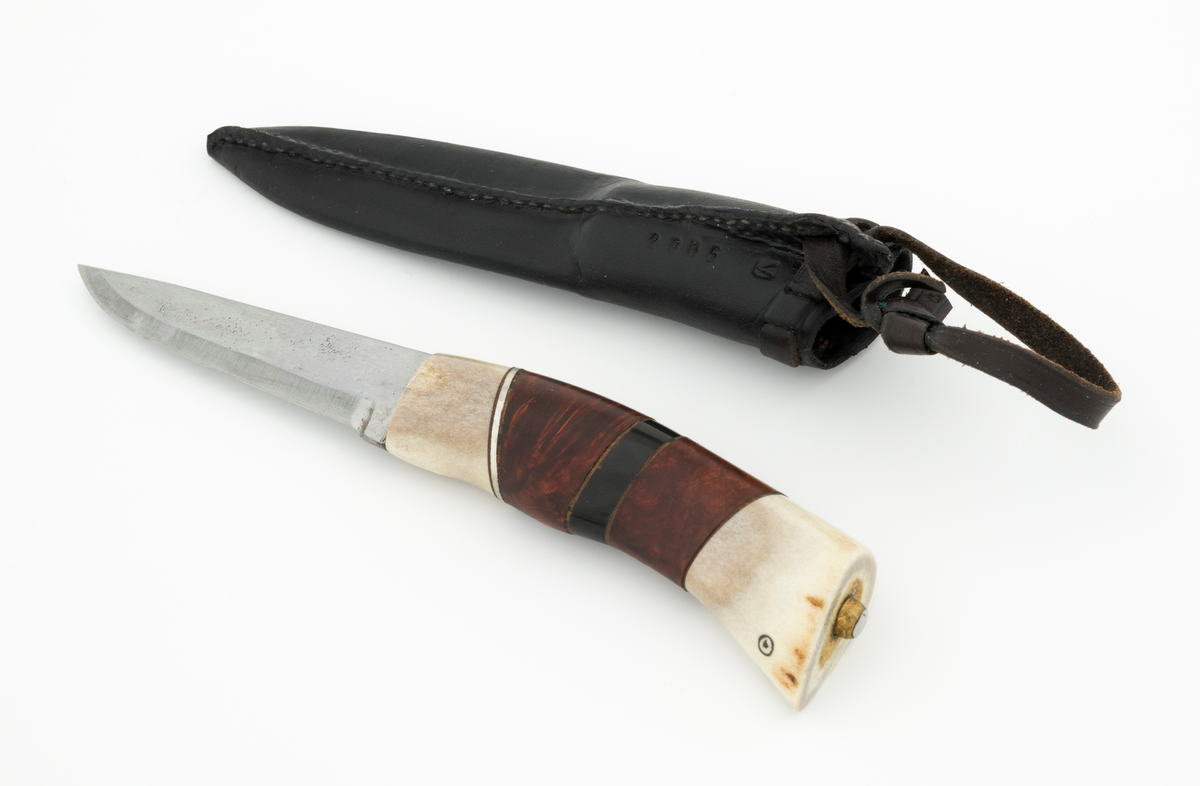 Tollekniv i slire, der knivskaftet og slira er lagd av den danske etnologen, museumslederen og knivmakeren Henrik Vensild, som i mange år besøkte Norsk skogmuseum og det såkalte «knivtorget» under De nordiske jakt- og fiskedager.

Kniven er 20,0 centimeter lang, målt fra bladspissen til og med knappen i ytterenden av skaftet. Bladet er 9,1 centimeter langt og snaut 2,3 centimeter bredt ved brystningen (overgangen til skaftet). Her er bladtjukkelsen om lag 3,7 millimeter, men den avtar noe framover mot knivspissen. Umiddelbart bak slipefasen der er tjukkelsen snaut 2,6 millimeter. Overflata på bladet har den noe rue overflata den fikk av hammeren på ambolten intakt, men disse flatene er polerte. Bakerst på høyre side finner vi et stempel, «Steen N.», som er stempelet til den danskfødte smeden Steen Nielsen, som lenge har bodd i Kristiansand. Bladryggen er planslipt, men er samtidig noe avrundet i den fremre enden. Slipefasene er opptil 6,5 millimeter brede.

Skaftet er nesten 10,5 centimeter langt. Det buer noe nedover (mot skaftbuken) i den bakre enden og har, som knivblader flest, et ovalt tverrsnitt. Sett i lengderetningen er den midtre delen av denne knivdelen noe konveks. Skaftet er sammensatt av flere komponenter. Fremst, mot bladet, er det en del av horn, antakelig reinsdyrgevir. Den enden som vender mot bladet er rett (butt), den andre enden er skrått avskåret. Mot denne flata er det lagt ei lærforing, deretter ei sølvplate og så nok ei lærforing. Deretter følger et stykke brunt, mønstret tre, en svart ring av et ibenholtliknende materiale. og nok et stykke av det brune, mønstrete treet. Ytterenden er skråskåret. På den skrå endeflata er det lagt nok ei lærforing, denne gangen uten noe metallinnlegg, mot endetappen, som er av reisdyrhorn. På denne komponenten er det to små ringer med et punkt i sentrum, en slags signatur for Henrik Vensild. Tangen fra knivbladet er ført gjennom hele skaftet. Den bakre enden av denne jernteinen er klinket mot noe som later til å være en messingring.

Slira er sydd av mørkebrunt lær. Den er cirka 16,9 centimeter lang (uten beltestropp) og 3,4 centimeter bred (målt på midten). Slireformen er symmetrisk, når man ser bort fra at overkanten er skrått avskåret. Den nedre delen, som skal omslutte bladet, er nokså flattrykt, mens den øvre delen, som skal omslutte nedre del av skaftet, er mer rundoval. Sliras forside er dekorert med to parallelle linjer i lengderetningen med innstemplete små treflikete blader med noenlunde regelmessig innbyrdes avstand. Dette dekorelementet er, åpenart med hensikt, plassert på en måte som bryter litt med den nevnte symmetrien. Like under sliremunningen er det skåret små spalter i slirelæret. Her er det inntredd ei cirka 9 millimeter bredt lærreim, som også er tredd gjennom ei spalte i et «øre» på den øvre delen av sliresømmen. Endene på den nevnte lærreima er knyttet sammen slik at den danner ei løkke som kan tres inn på et belte. Henrik Vensild har stemplet inn initialene sine og produksjonsåret - 2005 - på baksida av sliras overdel.