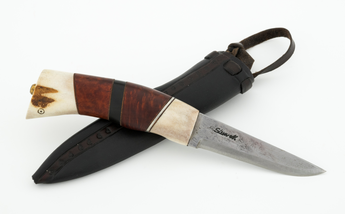 Tollekniv i slire, der knivskaftet og slira er lagd av den danske etnologen, museumslederen og knivmakeren Henrik Vensild, som i mange år besøkte Norsk skogmuseum og det såkalte «knivtorget» under De nordiske jakt- og fiskedager.

Kniven er 20,0 centimeter lang, målt fra bladspissen til og med knappen i ytterenden av skaftet. Bladet er 9,1 centimeter langt og snaut 2,3 centimeter bredt ved brystningen (overgangen til skaftet). Her er bladtjukkelsen om lag 3,7 millimeter, men den avtar noe framover mot knivspissen. Umiddelbart bak slipefasen der er tjukkelsen snaut 2,6 millimeter. Overflata på bladet har den noe rue overflata den fikk av hammeren på ambolten intakt, men disse flatene er polerte. Bakerst på høyre side finner vi et stempel, «Steen N.», som er stempelet til den danskfødte smeden Steen Nielsen, som lenge har bodd i Kristiansand. Bladryggen er planslipt, men er samtidig noe avrundet i den fremre enden. Slipefasene er opptil 6,5 millimeter brede.

Skaftet er nesten 10,5 centimeter langt. Det buer noe nedover (mot skaftbuken) i den bakre enden og har, som knivblader flest, et ovalt tverrsnitt. Sett i lengderetningen er den midtre delen av denne knivdelen noe konveks. Skaftet er sammensatt av flere komponenter. Fremst, mot bladet, er det en del av horn, antakelig reinsdyrgevir. Den enden som vender mot bladet er rett (butt), den andre enden er skrått avskåret. Mot denne flata er det lagt ei lærforing, deretter ei sølvplate og så nok ei lærforing. Deretter følger et stykke brunt, mønstret tre, en svart ring av et ibenholtliknende materiale. og nok et stykke av det brune, mønstrete treet. Ytterenden er skråskåret. På den skrå endeflata er det lagt nok ei lærforing, denne gangen uten noe metallinnlegg, mot endetappen, som er av reisdyrhorn. På denne komponenten er det to små ringer med et punkt i sentrum, en slags signatur for Henrik Vensild. Tangen fra knivbladet er ført gjennom hele skaftet. Den bakre enden av denne jernteinen er klinket mot noe som later til å være en messingring.

Slira er sydd av mørkebrunt lær. Den er cirka 16,9 centimeter lang (uten beltestropp) og 3,4 centimeter bred (målt på midten). Slireformen er symmetrisk, når man ser bort fra at overkanten er skrått avskåret. Den nedre delen, som skal omslutte bladet, er nokså flattrykt, mens den øvre delen, som skal omslutte nedre del av skaftet, er mer rundoval. Sliras forside er dekorert med to parallelle linjer i lengderetningen med innstemplete små treflikete blader med noenlunde regelmessig innbyrdes avstand. Dette dekorelementet er, åpenart med hensikt, plassert på en måte som bryter litt med den nevnte symmetrien. Like under sliremunningen er det skåret små spalter i slirelæret. Her er det inntredd ei cirka 9 millimeter bredt lærreim, som også er tredd gjennom ei spalte i et «øre» på den øvre delen av sliresømmen. Endene på den nevnte lærreima er knyttet sammen slik at den danner ei løkke som kan tres inn på et belte. Henrik Vensild har stemplet inn initialene sine og produksjonsåret - 2005 - på baksida av sliras overdel.