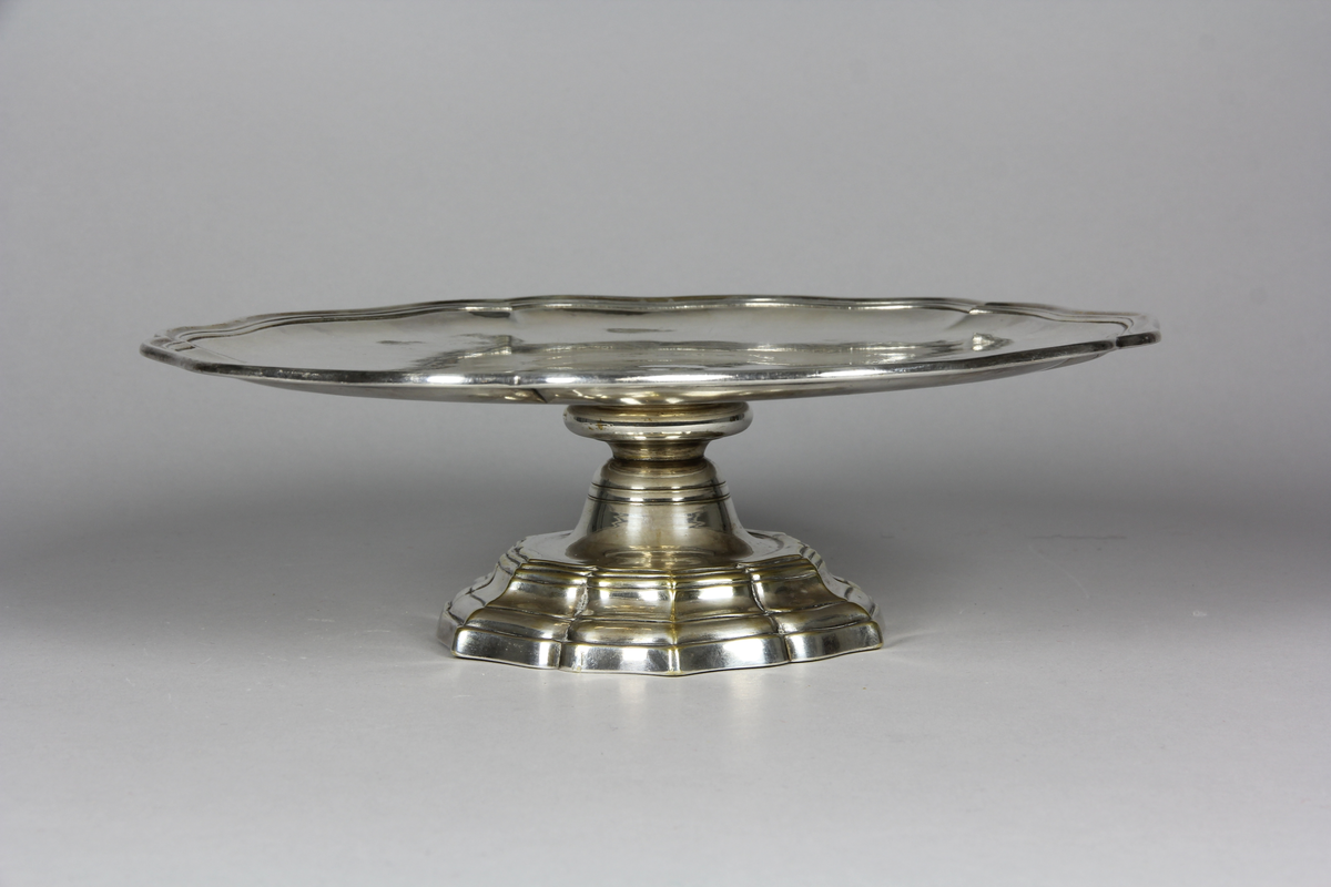 Bricka eller presenterbricka, en av ett par, sexpass form, utvikt kraftigt profilerat brötte och en slät spegel. Balusterformad fot med sexpass formad fotplatta.