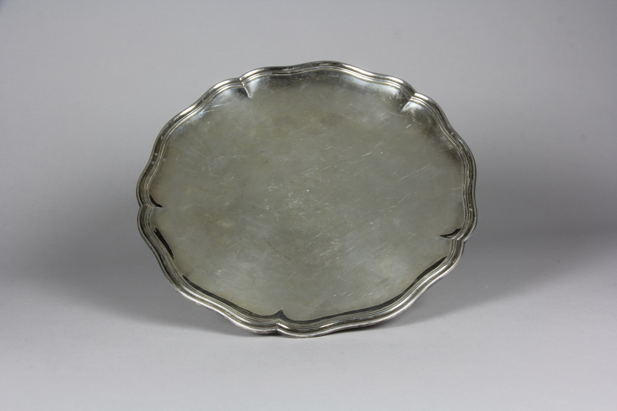 Bricka eller presenterbricka, en av ett par, sexpass form, utvikt kraftigt profilerat brötte och en slät spegel. Balusterformad fot med sexpass formad fotplatta.