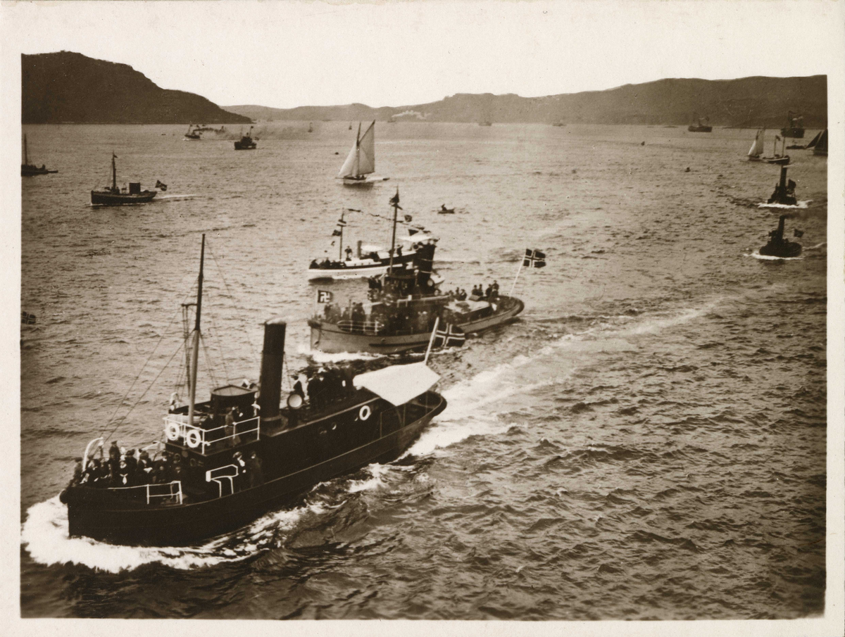 KRISTIANIAFJORD på vei inn til Bergen havn. En rekke småbåter følger dampskipet, én med hakekorsflagg.