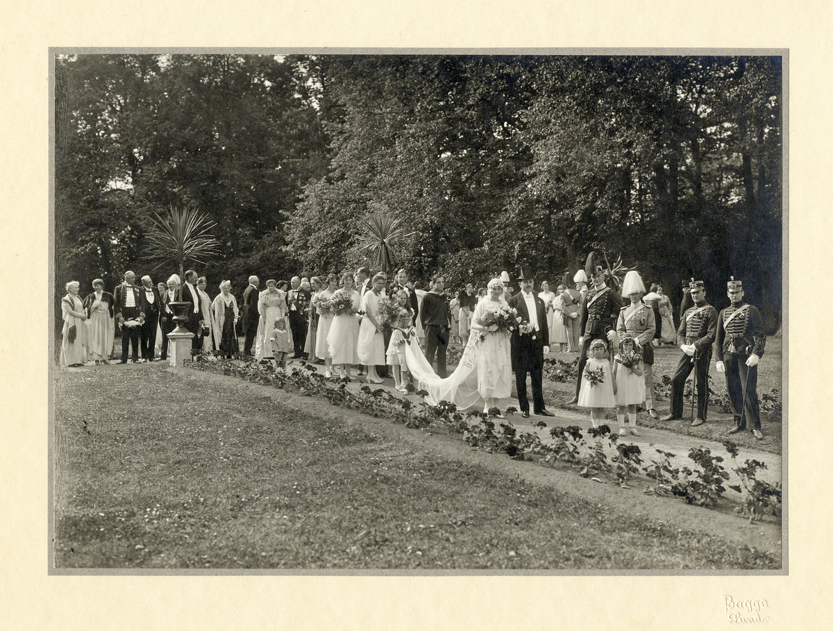 Ett societetsbröllop på Örtofta slott. 
Bröllop 19/5 1921 mellan fröken Stina-Brita Bennet, dotter t. friherren och godsägaren, ryttmästare Jacob Erland Bennet och h.h. Anna, f. Rosenblad, och greve Ove Thott. 
Brudparet är på väg genom slottsparken efter vigseln i Örtofta kyrka.