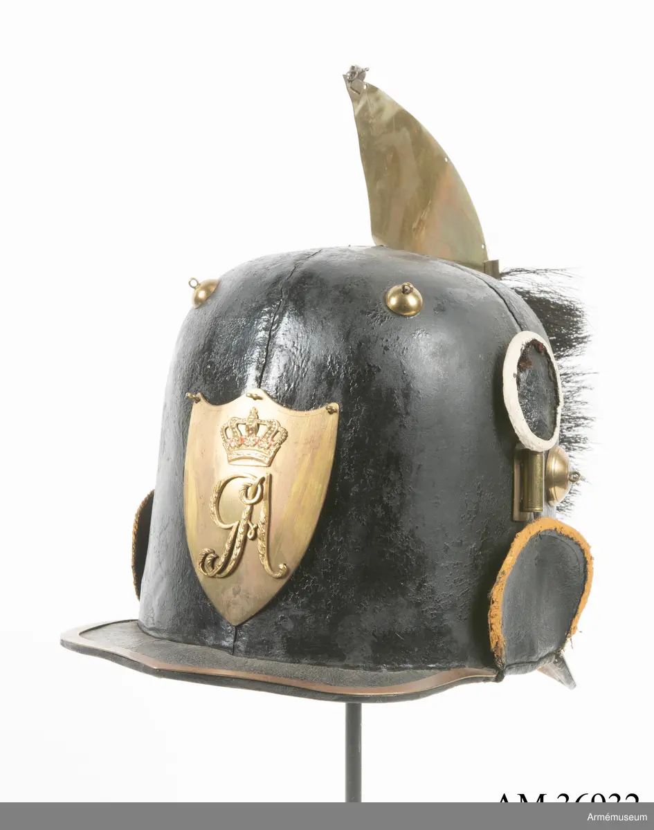 Kask med vapenplåt för manskap vid Västgöta (linje-)dragonregemente, troligen 1805-1807. Inrättad för plym som fattas. Vapenplåt med Gustaf IV Adolfs namnchiffer.