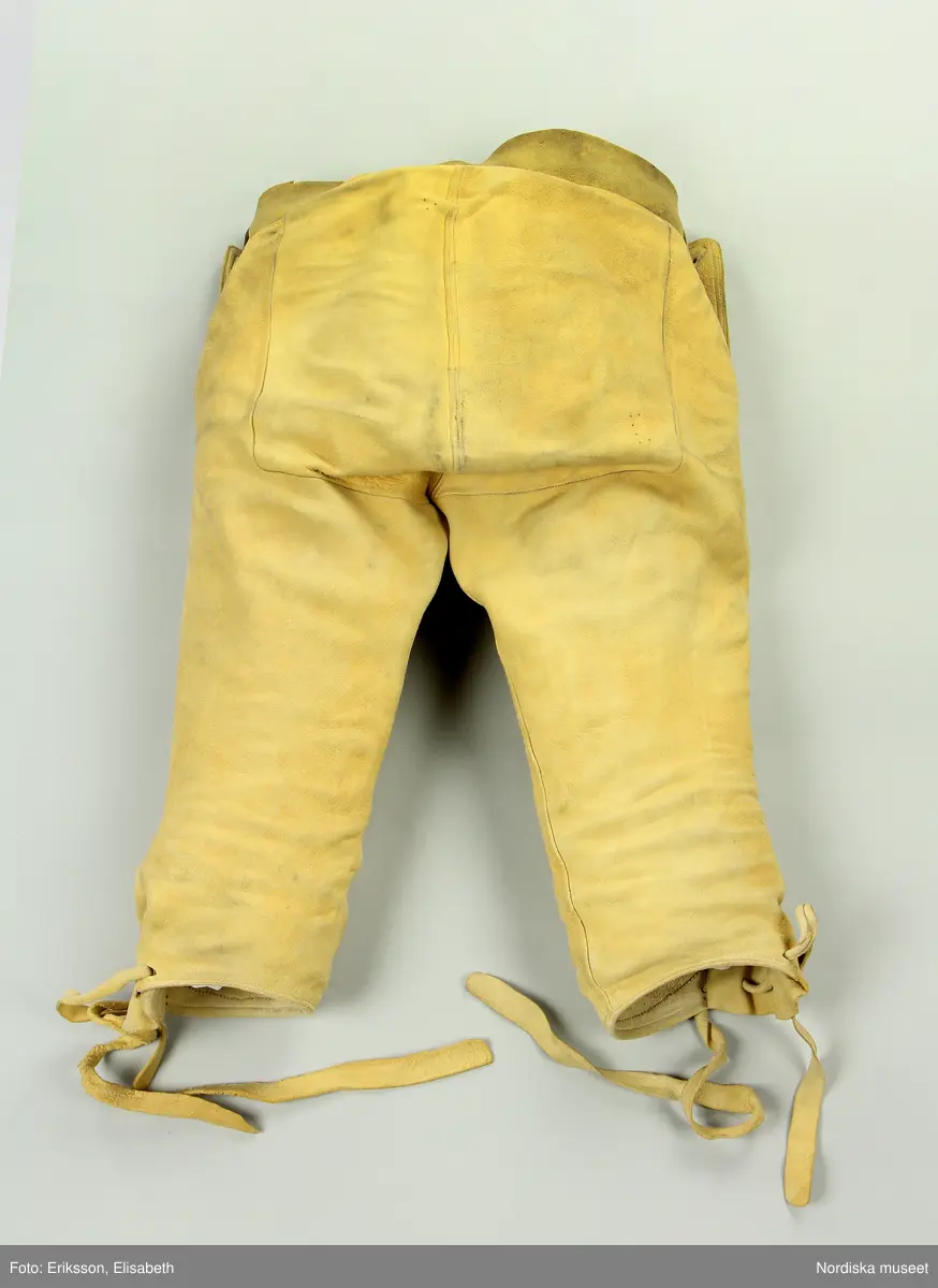 Hel mansdräkt bestående av 12 delar.
a. skjorta
b. rock av svart kläde
c. väst av svart kläde
d. knäbyxor av sämskskinn
e. förskinn
f. 1 par strumpor vita
g. handskar av sämsskinn
h. 1 par skor
i. hatt
j. hatt
k. långhalsduk
l. löskrage.
/BEEL

a. Mått: längd: 96 cm. Längd: 52 cm - ärmlängd. Vidd: 52 cm - ärmvidd
Material: Textil, linne. Lingarn - broderier, band. Teknik: Handvävning. Gåsögon. Trådbundet broderi. Broderi - plattsöm. Handsömnad
Rak mansskjorta i handvävt hellinnetyg, vävt i gåsögon.  Båltyget i ett stycke, sidosömmar med 13 cm långa sidosprund. Öppning fram, 31 cm långt sprund. Rektangulärt halsspjäll,  rynkningar mot 8,5 cm hög krage med broderier på både in- och utsida i kanten, plattsöm och trädsöm, nuggor i katnen. Två fastsydda mönstervävda knytband, blå/vit och vit. Vidsydd ärm med ärmspjäll. Rynkningar mot 1,3 cm bred ärmlinning broderad med plattsöm och trädsöm, nuggor i kanten,  mönstervävda knytband.. Skjortan är handsydd.
/Inga-Lill Eliasson 2007-04-17


f. 1 par strumpor  skaftlängd 40 cm, fot 26 cm; tvåändsstickade av vitt ullgarn i slätstickning.
g.
h.
i.
j.Hatt, svart rundkullig filthatt, kullens höjd 14 cm, brätte bredd 5 cm; lätt uppböjt brätte kantat med bomullsband, delvis fodrad med ljust bomullstyg.
/BEEL
k.Längd: 139 cm. Bredd: 18,5 cm. Material: Halvlinne. Telnik: Handvävning, dräll. Handsömnad.
Långhalsduk vävd i dräll, avlång,  randigt mönster av ca 1,3 cm breda ränder i dräll med tuskaft emellan. Handsydd smal fållad kant.
Anm: Något gulnad.
/INEL
l. Löskrage "hassdutj" längd 34 cm, bredd 8,7 cm, rak remsa av vit fin linnelärft, broderi i plattsöm längs långsidorna med små "nuggor" i kanten. Baksida av en bit linneväv med ränder i kypertvariation, knytband i ändarna av mönstervävt linneband i ljusgrått och vitt.

Berit Eldvik maj 2006