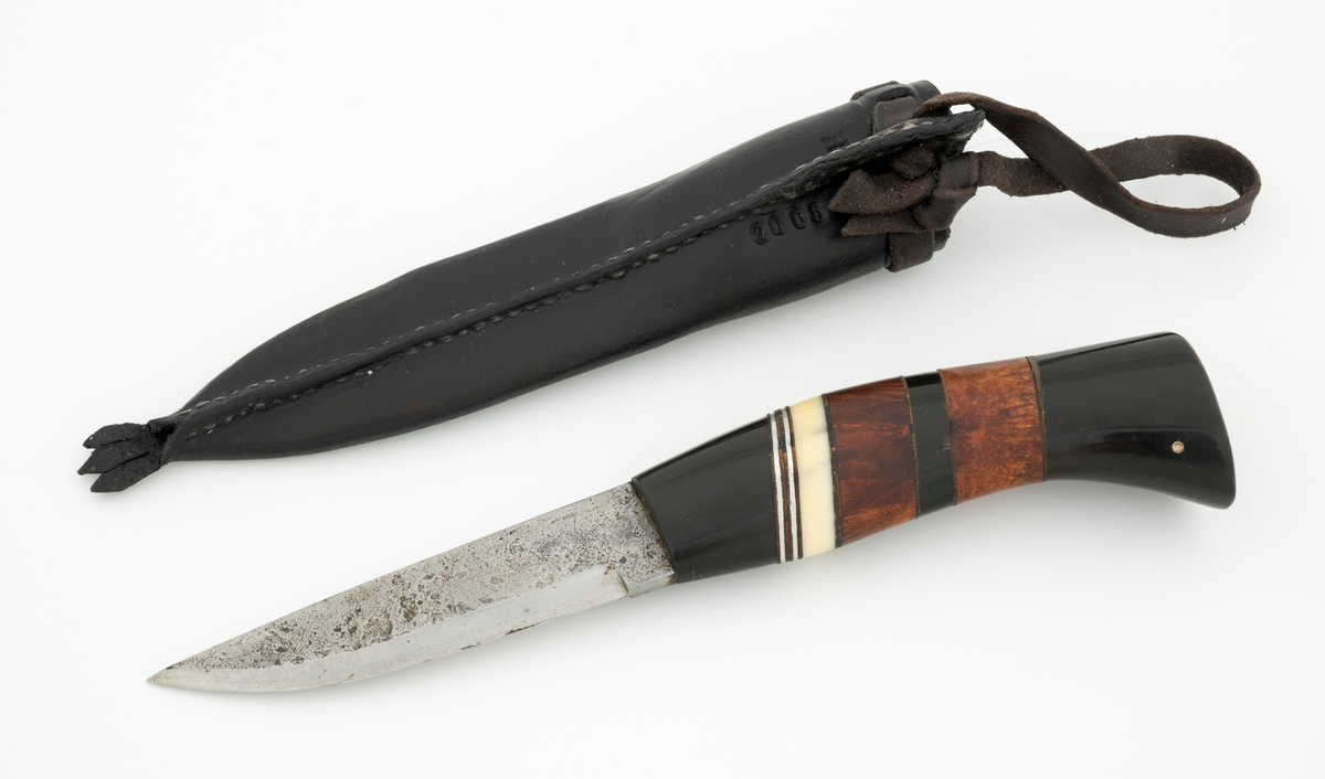 Tollekniv i slire, der knivskaftet og slira er lagd av den danske etnologen, museumslederen og knivmakeren Henrik Vensild, som i mange år besøkte Norsk skogmuseum og det såkalte «knivtorget» under De nordiske jakt- og fiskedager.

Kniven er 20,3 centimeter lang, målt fra bladspissen til og med knappen i ytterenden av skaftet. Bladet er 9,5 centimeter langt og 2,3 centimeter bredt ved brystningen (overgangen til skaftet). Her er bladtjukkelsen om lag 3,7 millimeter, men den avtar noe framover mot knivspissen. Umiddelbart bak slipefasen der er tjukkelsen 1,8 millimeter. Overflata på bladet har den noe rue overflata den fikk av hammeren på ambolten intakt, men disse flatene er polerte. Bakerst på høyre side finner vi et stempel, «JL», som er stempelet til smeden. Bladryggen er planslipt og en aning konveks i lengderetningen. Slipefasene er opptil 7,5 millimeter brede.

Skaftet er nesten 10,5 centimeter langt. Det buer noe nedover (mot skaftbuken) i den bakre enden og har, som knivblader flest, et ovalt tverrsnitt. Sett i lengderetningen er den fremre halvdelen av denne knivdelen noe konveks. Skaftet er sammensatt av flere komponenter. Fremst, mot bladet, er det en del av et svart, ibenholtliknende materiale. Den enden som vender mot bladet er rett (butt), den andre enden er skrått avskåret. Mot denne flata er det lagt ei lærforing, deretter ei sølvplate og så nok ei lærforing. Deretter følger ytterligere ei lærforing, ei sølvplate og nok ei lærforing. Så følger ei lys, cirka 6 millimeter bred hornskive. Så følger en bit i brunt tre, muligens briarrot, nok en bit av det svarte materialet og nok en bit av det brune treet. Ytterenden er også av det samme svarte materialet som vi finner i den fremre skaftenden. I denne komponenten er det inntappet to små sølvstaver, antakelig som en slags signatur for Henrik Vensild. Tangen fra knivbladet er ført gjennom hele skaftet. Den bakre enden av denne jernteinen er klinket mot noe som later til å være en messingring.

Slira er sydd av mørkebrunt lær. Den er cirka 18,4 centimeter lang (uten beltestropp) og 3,3 centimeter bred (målt på midten). Slireformen er symmetrisk, når man ser bort fra at overkanten er skrått avskåret. Den nedre delen, som skal omslutte bladet, er nokså flattrykt, mens den øvre delen, som skal omslutte nedre del av skaftet, er mer rundoval. Sliras forside er dekorert med linjer i lengderetningen og noe skrått på tvers. Mellom parallelle linjer der det innstemplet små treflikete blader med noenlunde regelmessig innbyrdes avstand. Dekorelementene er, åpenbart med hensikt, plassert på en måte som bryter litt med den nevnte symmetrien i sliras ytre form. Like under sliremunningen er det skåret små spalter i slirelæret. Her er det inntredd ei cirka 8,5 millimeter bredt lærreim, som også er tredd gjennom ei spalte i et «øre» på den øvre delen av sliresømmen. Endene på den nevnte lærreima er knyttet sammen slik at den danner ei løkke som kan tres inn på et belte. I den nedre enden av slira er det et trefliket dekorelement. Henrik Vensild har stemplet inn initialene sine og produksjonsåret - 2005 - på baksida av sliras overdel.