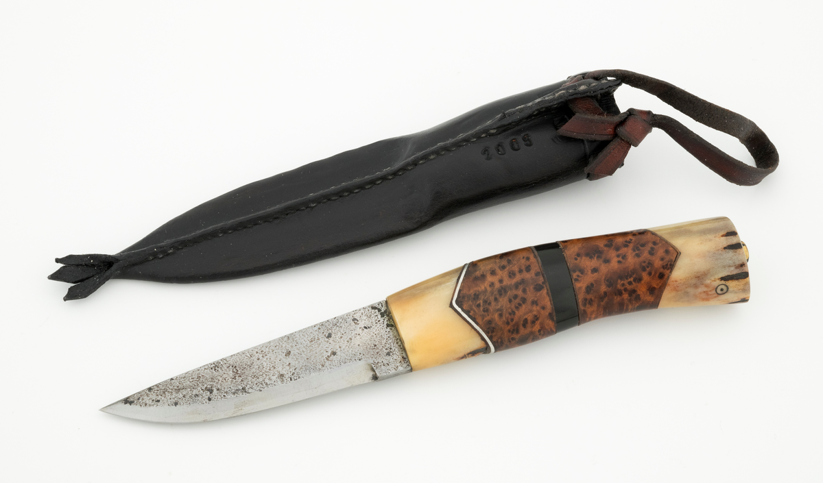 Tollekniv i slire, der knivskaftet og slira er lagd av den danske etnologen, museumslederen og knivmakeren Henrik Vensild, som i mange år besøkte Norsk skogmuseum og det såkalte «knivtorget» under De nordiske jakt- og fiskedager.

Kniven er 20,4 centimeter lang, målt fra bladspissen til og med knappen i ytterenden av skaftet. Bladet er 9,2 centimeter langt og snaut 2,5 centimeter bredt ved brystningen (overgangen til skaftet). Her er bladtjukkelsen om lag 3,7 millimeter, men den avtar noe framover mot knivspissen. Umiddelbart bak slipefasen der er tjukkelsen 2,4 millimeter. Overflata på bladet har den noe rue overflata den fikk av hammeren på ambolten intakt, men disse flatene er polerte. Bakerst på høyre side finner vi et stempel, bokstavene «JL», som antas å være initialene til smeden. Bladryggen er en liten aning konveks i lengderetningen. Slipefasene er opptil 7 millimeter brede.

Skaftet er nesten 10,8 centimeter langt. Det buer noe nedover (mot skaftbuken) i den bakre enden og har, som knivblader flest, et ovalt tverrsnitt. Sett i lengderetningen er den fremre delen konveks mens den bakre er konkav. Skaftet er sammensatt av flere komponenter. Fremst, mot bladet, er det en del av horn, antakelig reinsdyrgevir. Den enden som vender mot bladet er rett (butt), den andre enden er kappet i en «flat V-form». Mot denne flata er det lagt ei lærforing, deretter ei sølvplate og så nok ei lærforing. Så følger et stykke brunt, mønstret tre, en svart ring av et ibenholtliknende materiale. og nok et stykke av det brune, mønstrete trematerialet. Ytterenden av dette gjentar den «flate V-formen». På den sistnevnte endeflata er det lagt nok ei lærforing, denne gangen uten noe metallinnlegg, mot endetappen, som er av reinsdyrhorn. På denne komponenten er det to små ringer med et punkt i sentrum. Tangen fra knivbladet er ført gjennom hele skaftet. Den bakre enden av denne jernteinen er klinket mot noe som later til å være en messingring.

Slira er sydd av mørkebrunt lær. Den er cirka 18,9 centimeter lang (uten beltestropp) og 3,5 centimeter bred. Den delen av slira som skal omslutte bladet er symmetrisk i lengderetningen er har forsida et rutemønster (romber) med små kors i sentrum. Den øvre delen, som skal omslutte den nedre delen av knivskaftet, er glatt, med unntak av et litt asymmetrisk plassert belte med små stempler med treflikete blader i. Sliremunningen er noe skrått avskåret. Rundt denne delen av slira er det skåret små spalter som det er trukket en cirka 9 millimeter bred lærstrimmel gjennom. Denne strimmelen er også tredd gjennom ei spalte i en utposning på den øvre delen av sliresommen, der den er knyttet sammen til ei hempe som kan tres inn på et belte. Læret i opphenget har en noe lysere brunfarge enn den øvrige slira. Den nedre enden av slira avsluttes i et trefliket ornament. Henrik Vensild har stemplet inn initialene sine og produksjonsåret - 2005 - på baksida av sliras overdel.