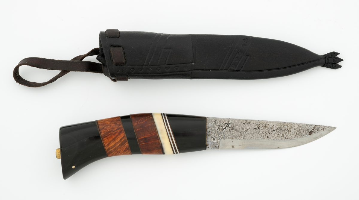 Tollekniv i slire, der knivskaftet og slira er lagd av den danske etnologen, museumslederen og knivmakeren Henrik Vensild, som i mange år besøkte Norsk skogmuseum og det såkalte «knivtorget» under De nordiske jakt- og fiskedager.

Kniven er 20,3 centimeter lang, målt fra bladspissen til og med knappen i ytterenden av skaftet. Bladet er 9,5 centimeter langt og 2,3 centimeter bredt ved brystningen (overgangen til skaftet). Her er bladtjukkelsen om lag 3,7 millimeter, men den avtar noe framover mot knivspissen. Umiddelbart bak slipefasen der er tjukkelsen 1,8 millimeter. Overflata på bladet har den noe rue overflata den fikk av hammeren på ambolten intakt, men disse flatene er polerte. Bakerst på høyre side finner vi et stempel, «JL», som er stempelet til smeden. Bladryggen er planslipt og en aning konveks i lengderetningen. Slipefasene er opptil 7,5 millimeter brede.

Skaftet er nesten 10,5 centimeter langt. Det buer noe nedover (mot skaftbuken) i den bakre enden og har, som knivblader flest, et ovalt tverrsnitt. Sett i lengderetningen er den fremre halvdelen av denne knivdelen noe konveks. Skaftet er sammensatt av flere komponenter. Fremst, mot bladet, er det en del av et svart, ibenholtliknende materiale. Den enden som vender mot bladet er rett (butt), den andre enden er skrått avskåret. Mot denne flata er det lagt ei lærforing, deretter ei sølvplate og så nok ei lærforing. Deretter følger ytterligere ei lærforing, ei sølvplate og nok ei lærforing. Så følger ei lys, cirka 6 millimeter bred hornskive. Så følger en bit i brunt tre, muligens briarrot, nok en bit av det svarte materialet og nok en bit av det brune treet. Ytterenden er også av det samme svarte materialet som vi finner i den fremre skaftenden. I denne komponenten er det inntappet to små sølvstaver, antakelig som en slags signatur for Henrik Vensild. Tangen fra knivbladet er ført gjennom hele skaftet. Den bakre enden av denne jernteinen er klinket mot noe som later til å være en messingring.

Slira er sydd av mørkebrunt lær. Den er cirka 18,4 centimeter lang (uten beltestropp) og 3,3 centimeter bred (målt på midten). Slireformen er symmetrisk, når man ser bort fra at overkanten er skrått avskåret. Den nedre delen, som skal omslutte bladet, er nokså flattrykt, mens den øvre delen, som skal omslutte nedre del av skaftet, er mer rundoval. Sliras forside er dekorert med linjer i lengderetningen og noe skrått på tvers. Mellom parallelle linjer der det innstemplet små treflikete blader med noenlunde regelmessig innbyrdes avstand. Dekorelementene er, åpenbart med hensikt, plassert på en måte som bryter litt med den nevnte symmetrien i sliras ytre form. Like under sliremunningen er det skåret små spalter i slirelæret. Her er det inntredd ei cirka 8,5 millimeter bredt lærreim, som også er tredd gjennom ei spalte i et «øre» på den øvre delen av sliresømmen. Endene på den nevnte lærreima er knyttet sammen slik at den danner ei løkke som kan tres inn på et belte. I den nedre enden av slira er det et trefliket dekorelement. Henrik Vensild har stemplet inn initialene sine og produksjonsåret - 2005 - på baksida av sliras overdel.