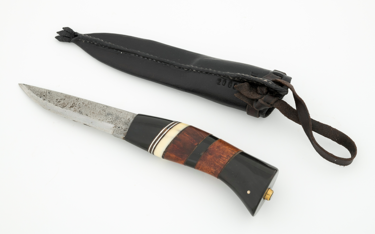 Tollekniv i slire, der knivskaftet og slira er lagd av den danske etnologen, museumslederen og knivmakeren Henrik Vensild, som i mange år besøkte Norsk skogmuseum og det såkalte «knivtorget» under De nordiske jakt- og fiskedager.

Kniven er 20,3 centimeter lang, målt fra bladspissen til og med knappen i ytterenden av skaftet. Bladet er 9,5 centimeter langt og 2,3 centimeter bredt ved brystningen (overgangen til skaftet). Her er bladtjukkelsen om lag 3,7 millimeter, men den avtar noe framover mot knivspissen. Umiddelbart bak slipefasen der er tjukkelsen 1,8 millimeter. Overflata på bladet har den noe rue overflata den fikk av hammeren på ambolten intakt, men disse flatene er polerte. Bakerst på høyre side finner vi et stempel, «JL», som er stempelet til smeden. Bladryggen er planslipt og en aning konveks i lengderetningen. Slipefasene er opptil 7,5 millimeter brede.

Skaftet er nesten 10,5 centimeter langt. Det buer noe nedover (mot skaftbuken) i den bakre enden og har, som knivblader flest, et ovalt tverrsnitt. Sett i lengderetningen er den fremre halvdelen av denne knivdelen noe konveks. Skaftet er sammensatt av flere komponenter. Fremst, mot bladet, er det en del av et svart, ibenholtliknende materiale. Den enden som vender mot bladet er rett (butt), den andre enden er skrått avskåret. Mot denne flata er det lagt ei lærforing, deretter ei sølvplate og så nok ei lærforing. Deretter følger ytterligere ei lærforing, ei sølvplate og nok ei lærforing. Så følger ei lys, cirka 6 millimeter bred hornskive. Så følger en bit i brunt tre, muligens briarrot, nok en bit av det svarte materialet og nok en bit av det brune treet. Ytterenden er også av det samme svarte materialet som vi finner i den fremre skaftenden. I denne komponenten er det inntappet to små sølvstaver, antakelig som en slags signatur for Henrik Vensild. Tangen fra knivbladet er ført gjennom hele skaftet. Den bakre enden av denne jernteinen er klinket mot noe som later til å være en messingring.

Slira er sydd av mørkebrunt lær. Den er cirka 18,4 centimeter lang (uten beltestropp) og 3,3 centimeter bred (målt på midten). Slireformen er symmetrisk, når man ser bort fra at overkanten er skrått avskåret. Den nedre delen, som skal omslutte bladet, er nokså flattrykt, mens den øvre delen, som skal omslutte nedre del av skaftet, er mer rundoval. Sliras forside er dekorert med linjer i lengderetningen og noe skrått på tvers. Mellom parallelle linjer der det innstemplet små treflikete blader med noenlunde regelmessig innbyrdes avstand. Dekorelementene er, åpenbart med hensikt, plassert på en måte som bryter litt med den nevnte symmetrien i sliras ytre form. Like under sliremunningen er det skåret små spalter i slirelæret. Her er det inntredd ei cirka 8,5 millimeter bredt lærreim, som også er tredd gjennom ei spalte i et «øre» på den øvre delen av sliresømmen. Endene på den nevnte lærreima er knyttet sammen slik at den danner ei løkke som kan tres inn på et belte. I den nedre enden av slira er det et trefliket dekorelement. Henrik Vensild har stemplet inn initialene sine og produksjonsåret - 2005 - på baksida av sliras overdel.