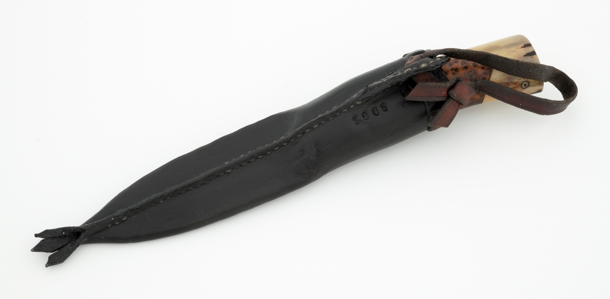 Tollekniv i slire, der knivskaftet og slira er lagd av den danske etnologen, museumslederen og knivmakeren Henrik Vensild, som i mange år besøkte Norsk skogmuseum og det såkalte «knivtorget» under De nordiske jakt- og fiskedager.

Kniven er 20,4 centimeter lang, målt fra bladspissen til og med knappen i ytterenden av skaftet. Bladet er 9,2 centimeter langt og snaut 2,5 centimeter bredt ved brystningen (overgangen til skaftet). Her er bladtjukkelsen om lag 3,7 millimeter, men den avtar noe framover mot knivspissen. Umiddelbart bak slipefasen der er tjukkelsen 2,4 millimeter. Overflata på bladet har den noe rue overflata den fikk av hammeren på ambolten intakt, men disse flatene er polerte. Bakerst på høyre side finner vi et stempel, bokstavene «JL», som antas å være initialene til smeden. Bladryggen er en liten aning konveks i lengderetningen. Slipefasene er opptil 7 millimeter brede.

Skaftet er nesten 10,8 centimeter langt. Det buer noe nedover (mot skaftbuken) i den bakre enden og har, som knivblader flest, et ovalt tverrsnitt. Sett i lengderetningen er den fremre delen konveks mens den bakre er konkav. Skaftet er sammensatt av flere komponenter. Fremst, mot bladet, er det en del av horn, antakelig reinsdyrgevir. Den enden som vender mot bladet er rett (butt), den andre enden er kappet i en «flat V-form». Mot denne flata er det lagt ei lærforing, deretter ei sølvplate og så nok ei lærforing. Så følger et stykke brunt, mønstret tre, en svart ring av et ibenholtliknende materiale. og nok et stykke av det brune, mønstrete trematerialet. Ytterenden av dette gjentar den «flate V-formen». På den sistnevnte endeflata er det lagt nok ei lærforing, denne gangen uten noe metallinnlegg, mot endetappen, som er av reinsdyrhorn. På denne komponenten er det to små ringer med et punkt i sentrum. Tangen fra knivbladet er ført gjennom hele skaftet. Den bakre enden av denne jernteinen er klinket mot noe som later til å være en messingring.

Slira er sydd av mørkebrunt lær. Den er cirka 18,9 centimeter lang (uten beltestropp) og 3,5 centimeter bred. Den delen av slira som skal omslutte bladet er symmetrisk i lengderetningen er har forsida et rutemønster (romber) med små kors i sentrum. Den øvre delen, som skal omslutte den nedre delen av knivskaftet, er glatt, med unntak av et litt asymmetrisk plassert belte med små stempler med treflikete blader i. Sliremunningen er noe skrått avskåret. Rundt denne delen av slira er det skåret små spalter som det er trukket en cirka 9 millimeter bred lærstrimmel gjennom. Denne strimmelen er også tredd gjennom ei spalte i en utposning på den øvre delen av sliresommen, der den er knyttet sammen til ei hempe som kan tres inn på et belte. Læret i opphenget har en noe lysere brunfarge enn den øvrige slira. Den nedre enden av slira avsluttes i et trefliket ornament. Henrik Vensild har stemplet inn initialene sine og produksjonsåret - 2005 - på baksida av sliras overdel.