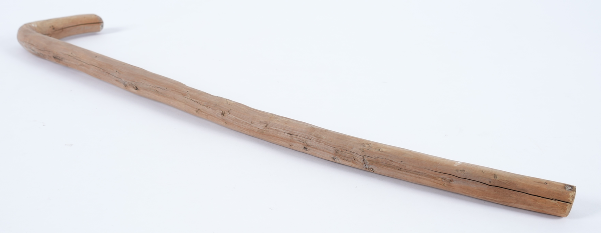 Spaserstokk utskoren av eit stykke einer. Naturvaksen L-form med vinkel til handtak på den eine enden. Stokken har rundt tverrsnitt. Berken var fjerna.