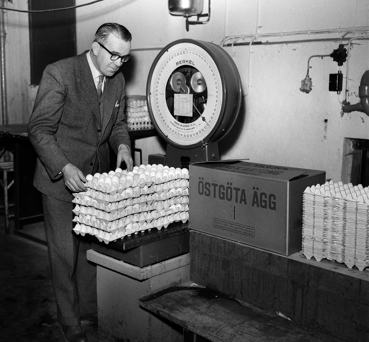 Ett dussin tjogplattor med ägg vägs vid Östgöta Äggs anläggning i Linköping 1956. På bilden disponent Jonas Lundberg som hjälpte fotografen att göra uppdraget mer livfullt. Företagets anläggning bar dåvarande adressen Köpetorpsvägen 1, vilket senare motsvarade tomten till Biltemas gamla butik och sedermera lager, Torvingegatan 2. De sista resterna av Östgöta Ägg revs under 1980-talet.