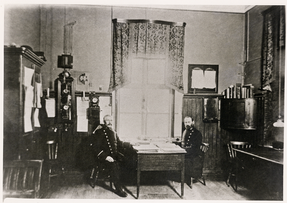 Interiör från polisstationen i Växjö 1904, i nuvarande stadshotellet. Vid skrivbordet sitter överkonstapel Carl Johansson och poliskonstapel J P Bergström.