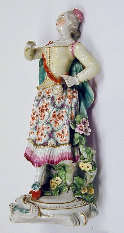 Porselensfigur, kvinne med kappe og veske.