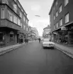 Nygatan ned mot Trädgårdstorget i Linköping. Bortom korsande Klostergatan har stora förändringar skett sedan bilden togs 1963 eller möjligtvis 1964. I övrigt är miljön lätt igenkännbar för den som är förtrogen med staden.