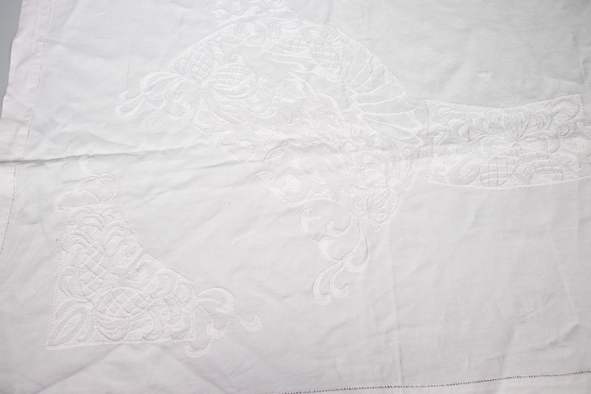 Rektangulær duk med brodert mønster med hvit tråd. Noen små hull etter slitasje. 
