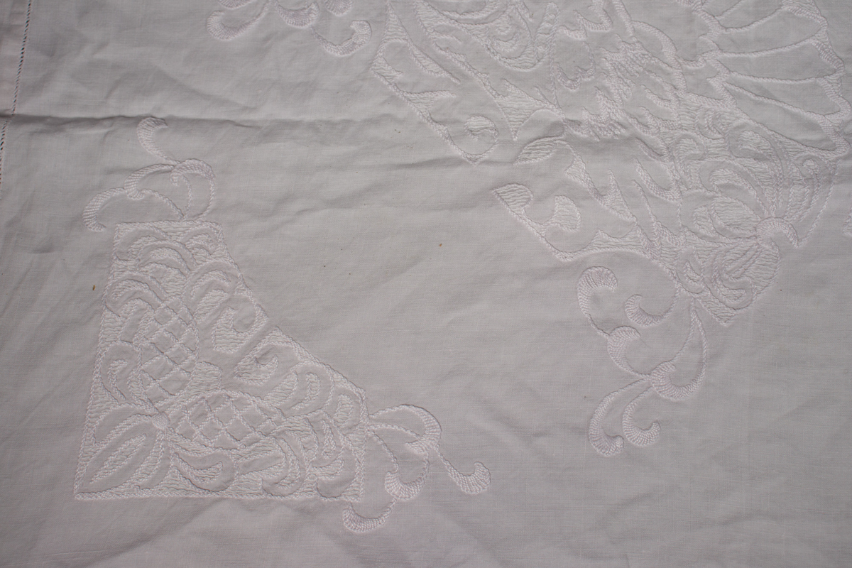 Rektangulær duk med brodert mønster med hvit tråd. Noen små hull etter slitasje. 