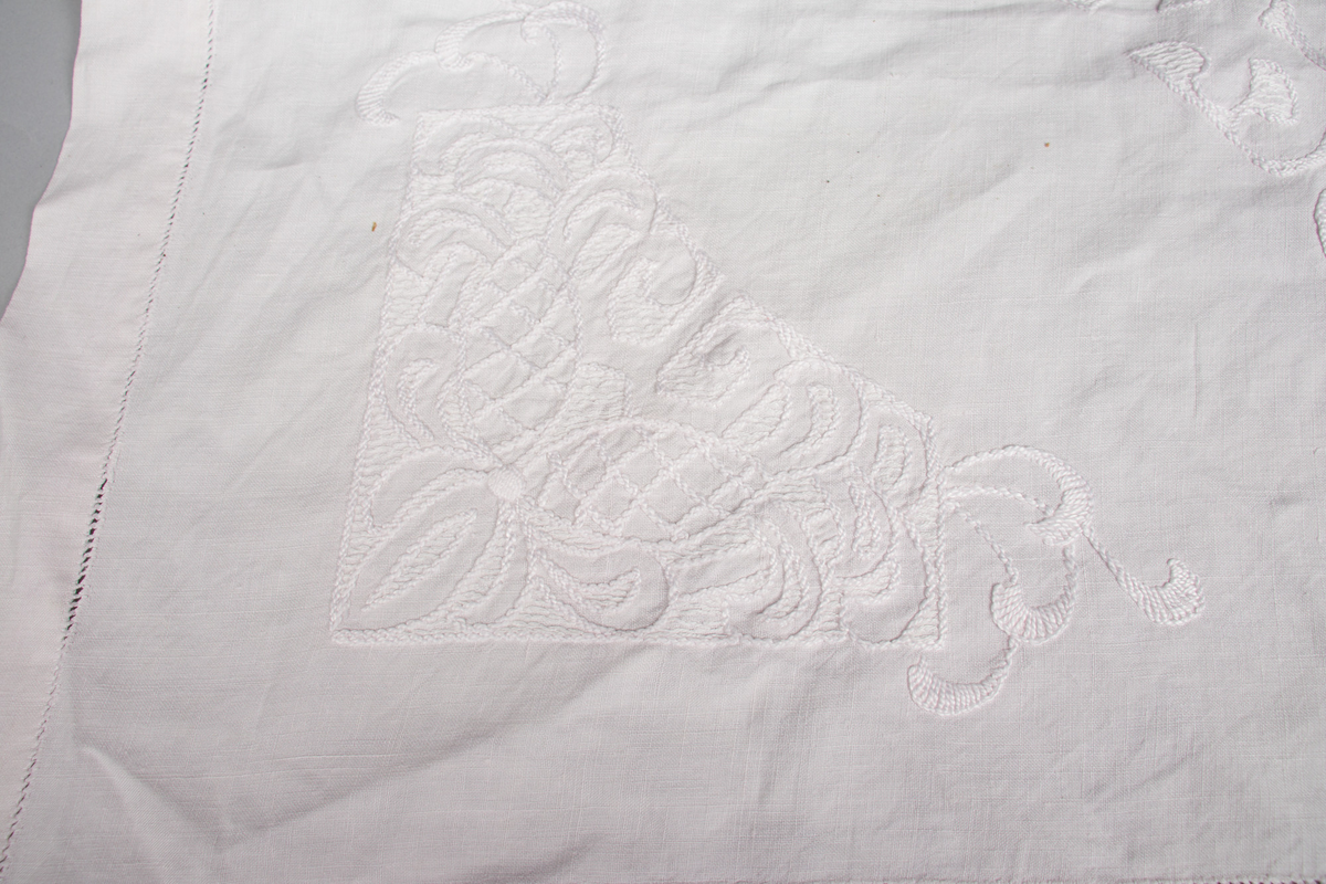 Rektangulær duk med brodert mønster med hvit tråd. Noen små hull etter slitasje. 