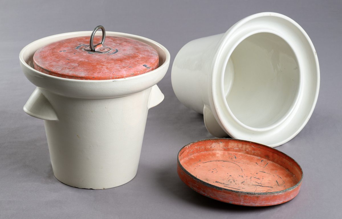 Latrinkärl, 2 st. Vitt porslin med lock i orangemålad plåt. Kärlen har individuell numrering, 33 respektive 48 (möjligen cellnumrering). 
Kärlen samhör med latrinhiss V 4700034.