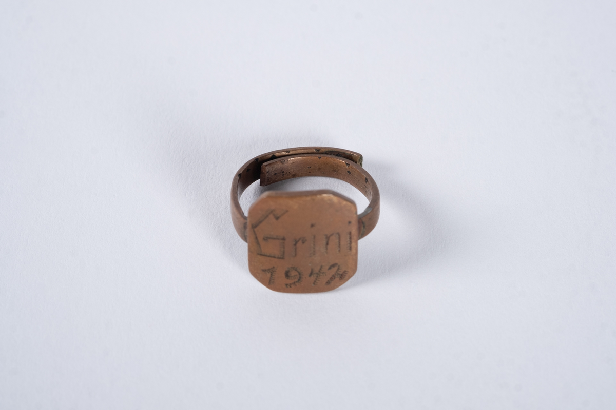Justerbar ring med åttekantet plate. Det er inngravert tekst og tall på platen. 