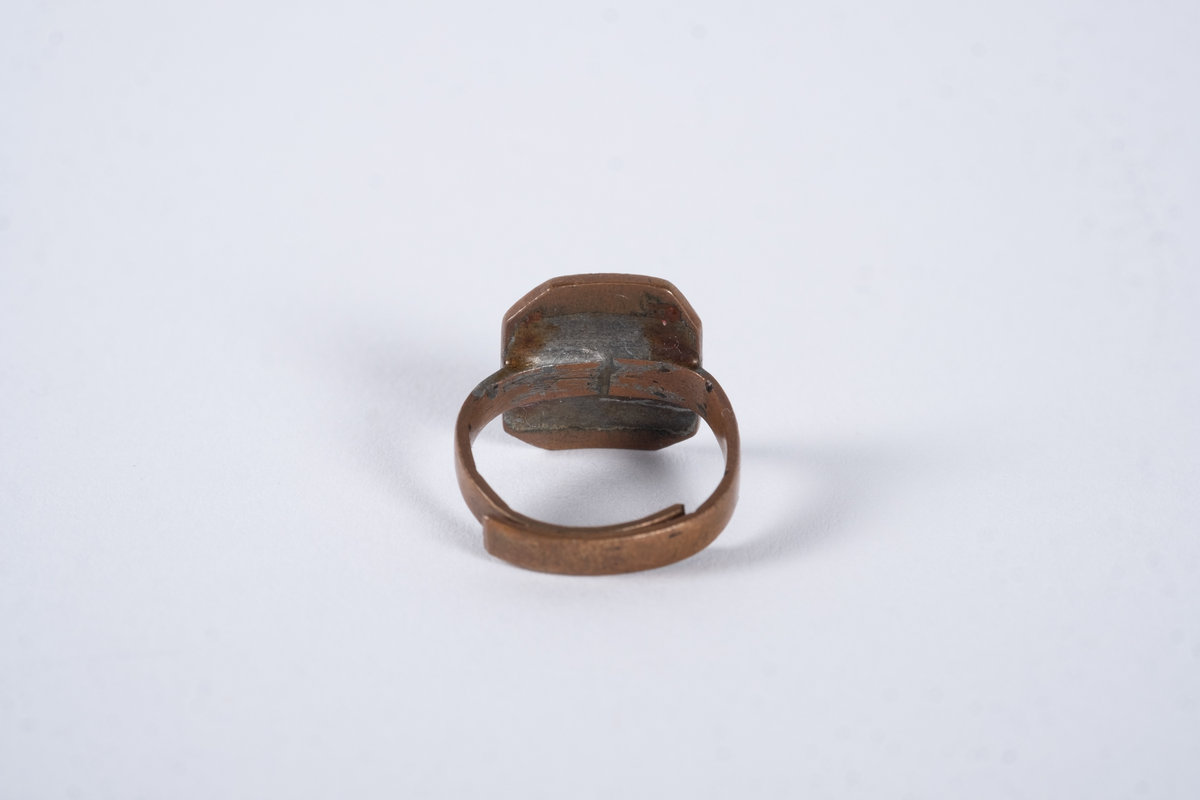 Justerbar ring med åttekantet plate. Det er inngravert tekst og tall på platen. 