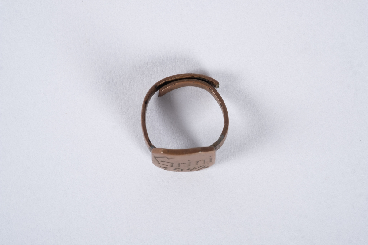 Justerbar ring med åttekantet plate. Det er inngravert tekst og tall på platen. 
