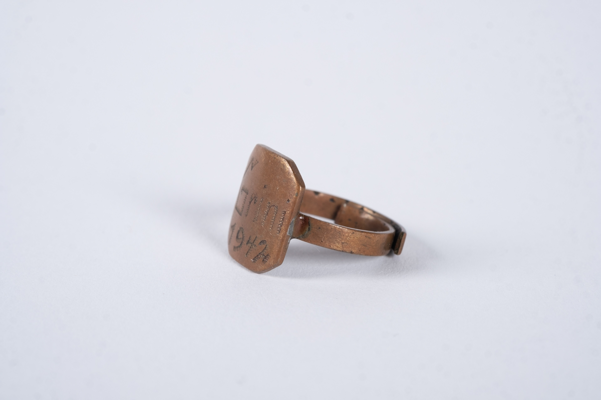 Justerbar ring med åttekantet plate. Det er inngravert tekst og tall på platen. 