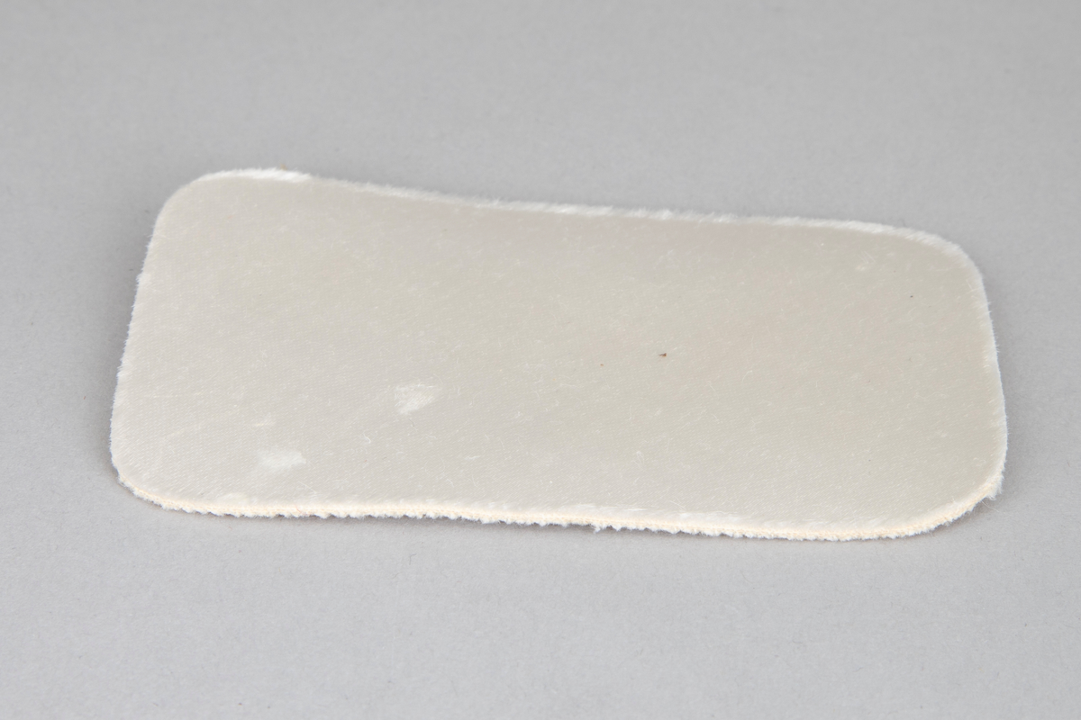 Hvite satengsko, med bred ringning, butt tå, slingback/hælstropp og kraftig, silketrukket hæl med moderat høyde. Lys brun lærlignende såle og svart gummi- eller plastlignende flikk. Ringning og slingback kantet med smalt ripsbånd og hælstroppen fôret med syntetskinn. Gulnet, kypertvevd tekstil innside. Innvendig, hvit såle av plastbelagt lerretsvev klebet på tynn papp. Den innvendige sålen er løsnet i limingen, og man kan se et løst, hælformet, hvitt papir eller vlieselinlag mellom den og selve hælen. Dette for å skjule, hindre ubehag fra de 4 spikre som hælen er festet med. Str 6, dvs 39. Ingen regulering på hælstroppen, men det er festet en flat strikk midt bak, som holder stroppen inntil hælen.