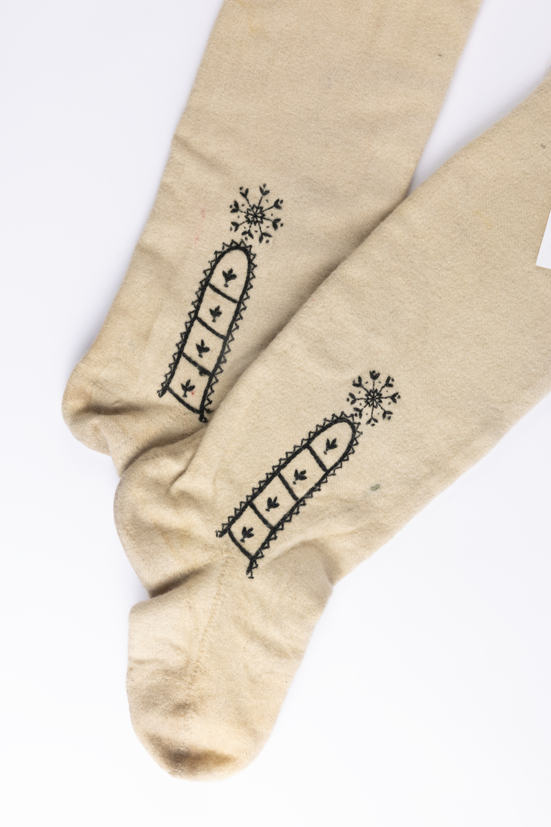 Hvite sydde strømper av vadmel med brodert dekor i svart.