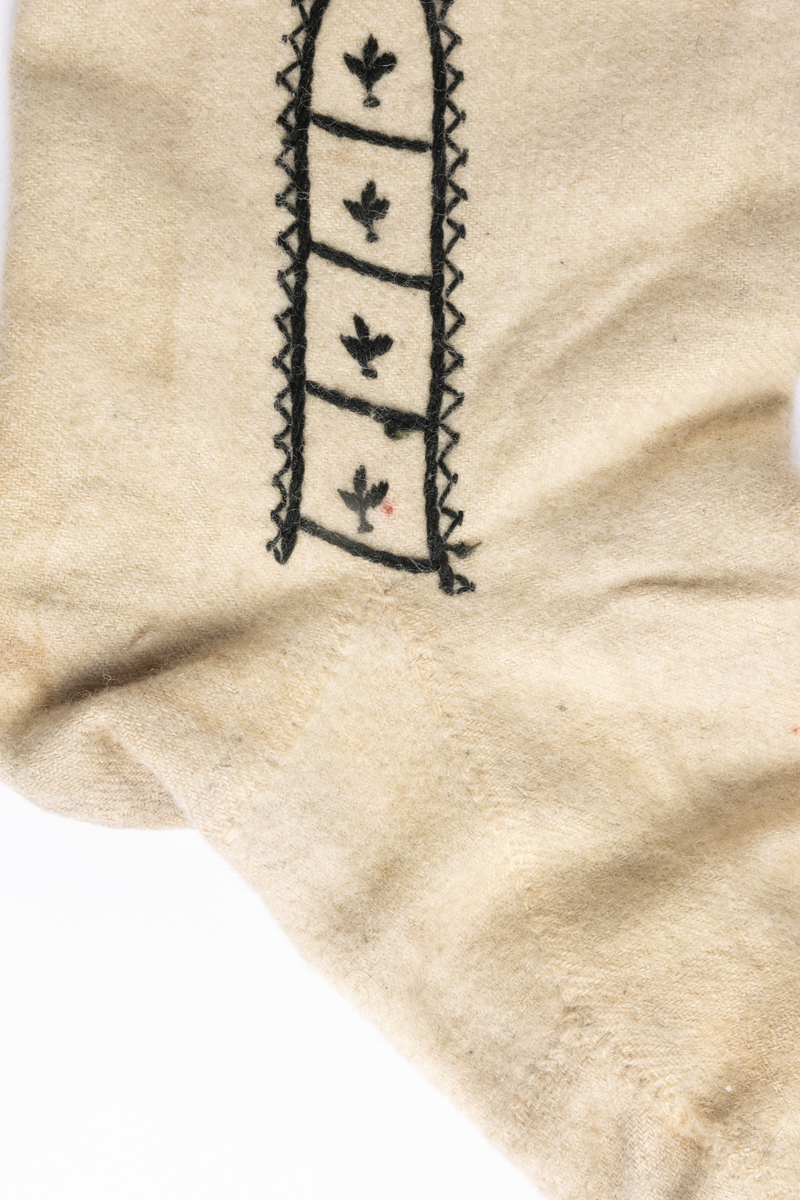 Hvite sydde strømper av vadmel med brodert dekor i svart.