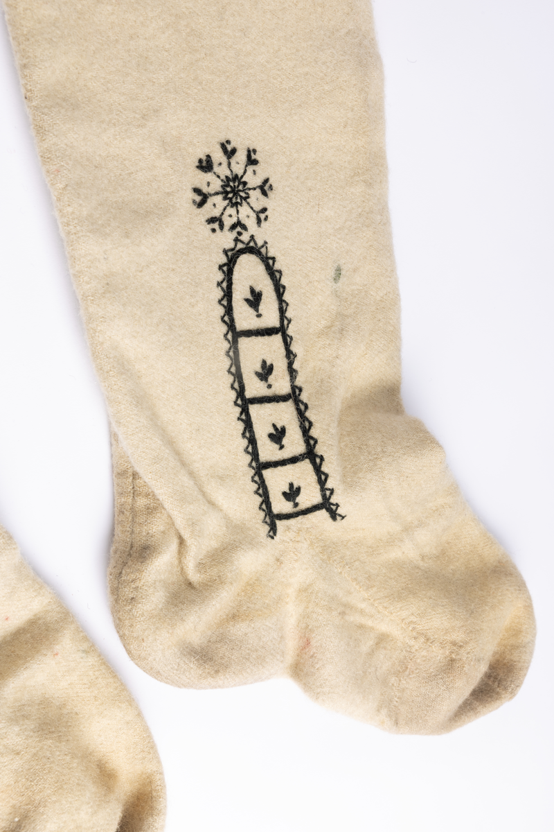 Hvite sydde strømper av vadmel med brodert dekor i svart.