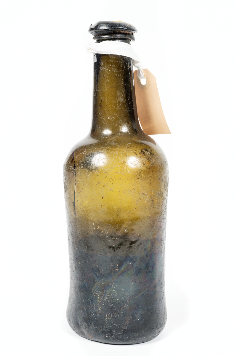 Vinflaska av mörkgrönt glas, delvis fylld med vätska.