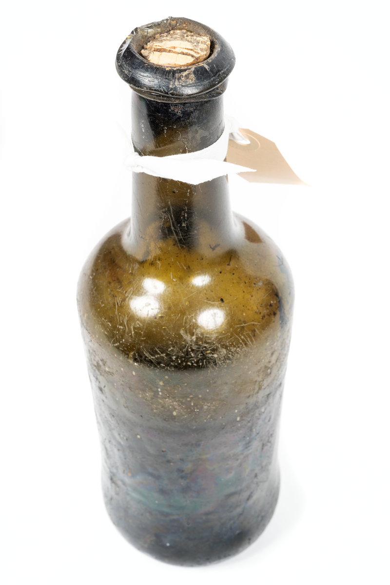 Vinflaska av mörkgrönt glas, delvis fylld med vätska.