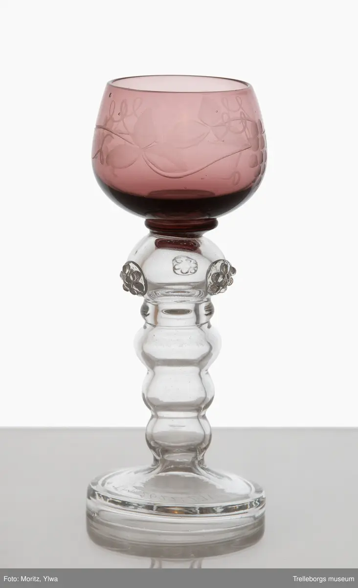 Liten remmare till likör.
Klarglas, fot ofärgad, kupa lila. Slipad dekor av vinrankor på kupan.