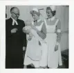 Foto på dopdag för Nils-Åke med pastor Bäckström, barnsköterskan Margit Forsell som håller i gossen samt en till barnsköterska.