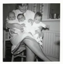 Fotografi på en barnsköterska med tre småttingar i sitt knä 