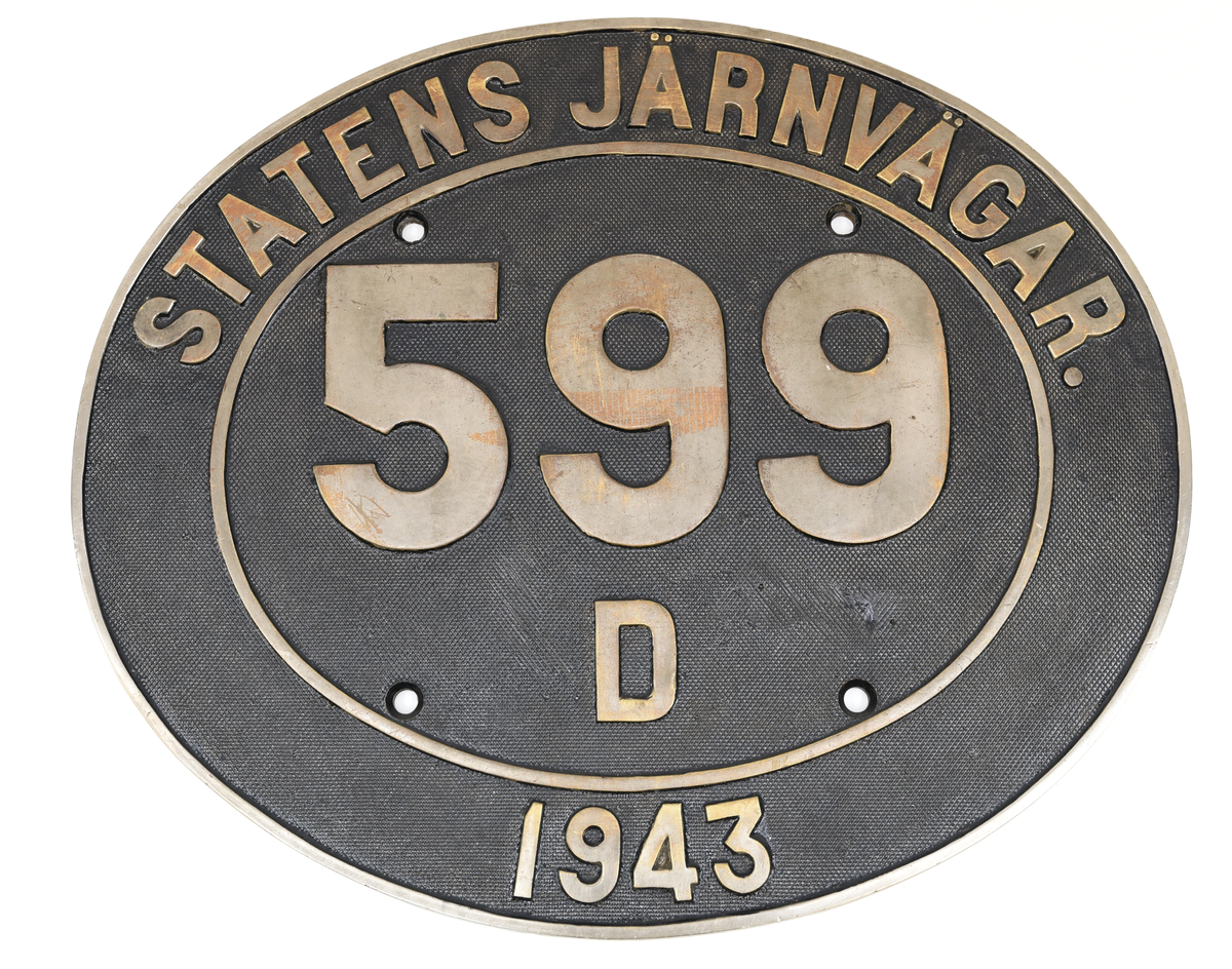 Oval loknummerskylt i svart och grå metall. Skylten bär texten "Statens Järnvägar 599 D 1943". Skylten har fyra upphängningshål.